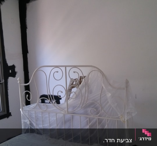 הכנת חדר שינה מרוהט ומיטה מכוסה בניילון לקראת צביעת קירות